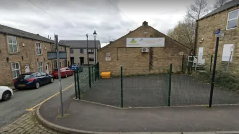 Google A Google Streetview screengrab of Cornerhouse Day Nursery in Lees. It is a brick building with a paved area outside and a fence running around the perimeter.