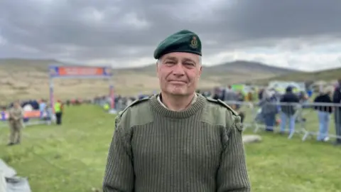 Major Dave Pickering smiling at the camera and stood in front of the finish line.