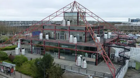 The reflective glass pyramid structure that is The Point in Milton Keynes. It has its edges lined by red metal frames.
