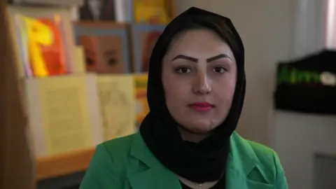 Almas Ipswich Feriba Almas wearing a black hijab and a green blazer. She is looking into the camera and not smiling 