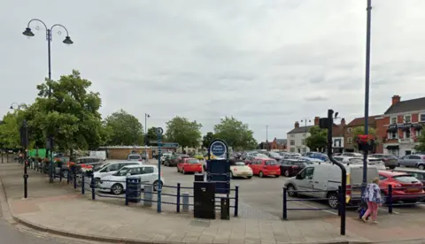 Google Google view of the Cattle Market car park in Boston. There are cars parked in the bays and buildings in the background. There is a sign with the name of the car park on it.