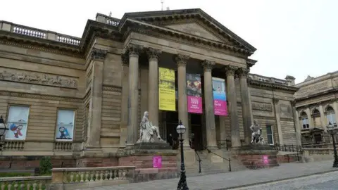 JeremyBolwell/Geograph The Georgian facade of the Walker Art Gallery looms over the centre of Liverpool. Street lights, statues and ornate stone fences can be seen.