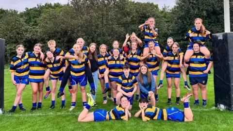 A group photo of the North Somerset Barbarians rugby team. They are all wearing their yellow, black and blue striped rugby uniform. 