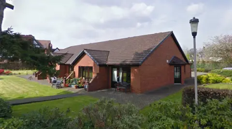 Google A single-storey red brick building with a surrounding garden