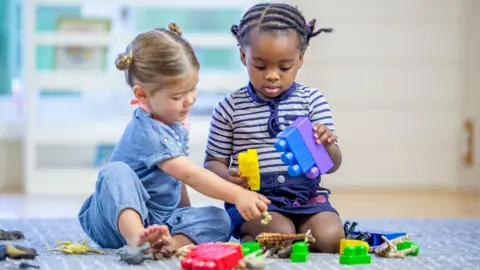 Stock image of two toddlers - one girl and one boy - playing with toy bricks on a carpet