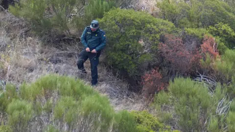 PA Media A Guardia Civil officer in green uniform descends down a ravine