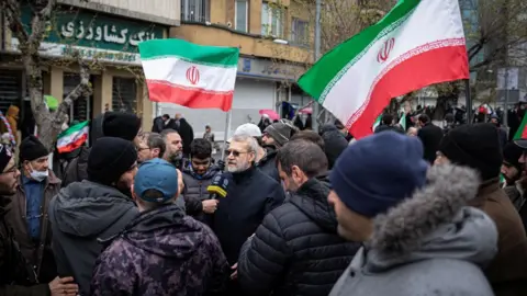 Ali Larijani via X/via REUTERS A social media photo posted by Ali Larijani showing him speaking to Iranian TV while taking part in a pro-government Quds Day rally in Tehran, Iran (13 March 2026)