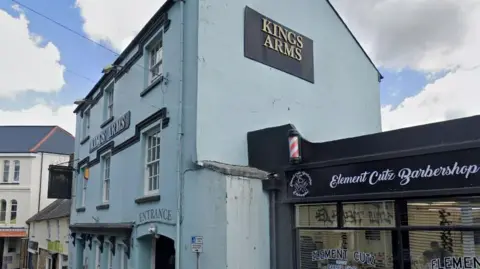 Google Street View image from outside The Kings Arms in Okehampton, which has light blue walls and signs with Kings Arms written in gold lettering on a black sign.