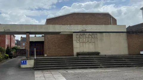 The front of the Octagon Chapel with its name and above that a sign saying Antiques Saleroom