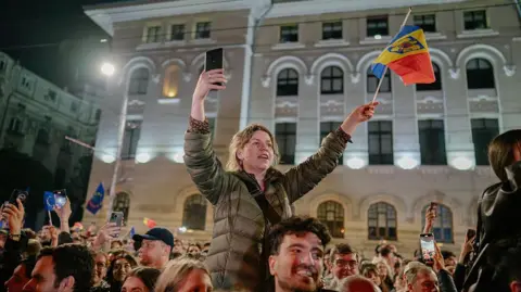 Getty Images A woman sits on a man's shoulders waving a Romanian flag