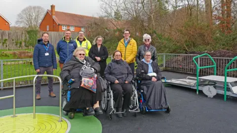 Salisbury City Council A group of adults of varying ages in a park smiling at a camera. Three are in wheelchairs and others stand behind them.