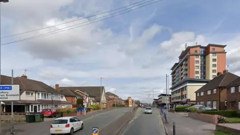 A road with a row of houses to the left side, and housing and tower blocks on the right