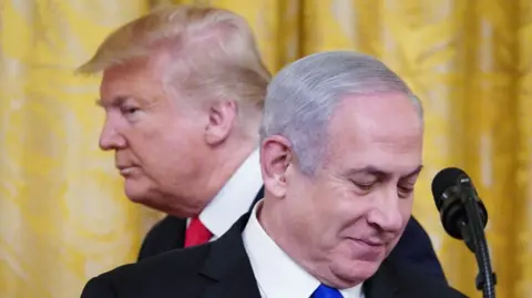 Photo showing US president Donald Trump and Israeli Prime Minister Benjamin Netanyahu. Behind them is a yellow curtain. Trump is behind Netanyahu facing left. Netanyahu is face on and looking down at a piece of paper.