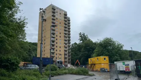 LDRS Image of dilapidated high rise block of floats with construction vehicles and a mechanical digger nearby.