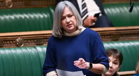 Parlamento do Reino Unido Liz Saville Roberts na Câmara dos Comuns. Ela está usando um top azul e um relógio de cor escura