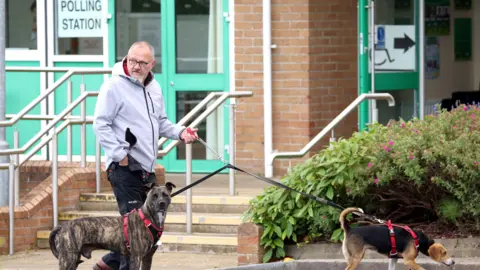 Pacemaker A man in a grey jacket standing outside a polling station with two dogs on leads