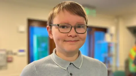 Dougie, a 13-year-old with light brown hair and glasses gives a slight smile as he attends the Climate Café in Dunkeld.