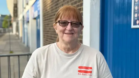 Cameron Noble/BBC A head and shoulders image of Deborah Marshall He is wearing a white T-shirt and dark sunglasses. He is standing in front of Portman Road and looking into the camera.
