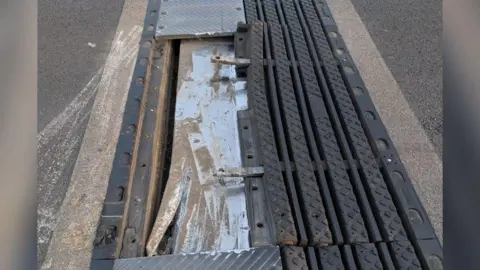 National Highways A close-up of a damaged metal joint along a motorway. The metal of the joint has been taken away and several parts are sticking out.