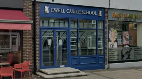 A blue shop front for Ewell Castle School on the high street, between a Costa Coffee and a nail bar