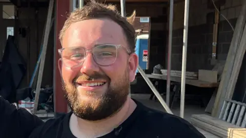 Tobey Newall in a black t-shirt and glasses looking at camera.