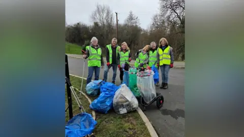 Carol Ludwig A group of litter-pickers in high-vis jackets standing around empty bags of rubbish.