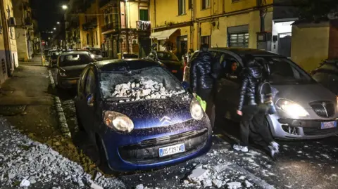 A car with the front bonnet and windscreen crushed under rocks and rubble.