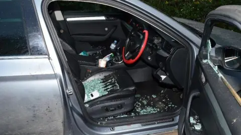Cambs Police The driver's side of a car has a smashed window. The door is open and there is shattered glass all over the seat the the footwell. The steering wheel has a red rim