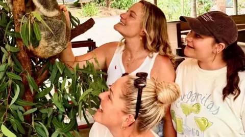 Mickey Drew A picture of three people smiling and looking at a koala in a tree.