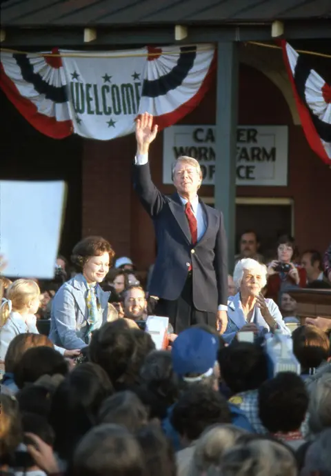 Corbis/Getty Images Presidenti i sapozgjedhur Jimmy Carter me gruan dhe nënën e tij përshëndet turmën e mbështetësve në një tubim fitoreje në qytetin e tij të lindjes, Plains Georgia