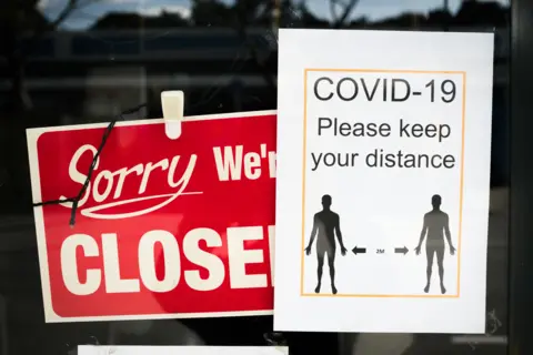 Getty Images A red sign saying sorry we're closed beside another sign warning of required Covid distancing