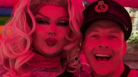Isobel Heely Maya Punion (L) and Captain Smash (R) posing for the camera and looking happy during the event. Maya has curly blonde hair and a nose ring, while Captain Smash has a captain's hat on.