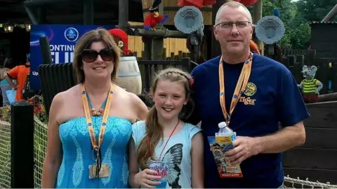 Lawson family Jessica Lawson stands between her parents Brenda and Tony at a theme park. Jessica wears a blue top with butterfly design, Brenda wears a blue dress and dark sunglasses and Tony weaers a dark-blue T-shirt.