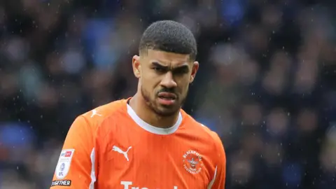 Ashley Fletcher playing for Blackpool in their orange kit, on a rainy afternoon