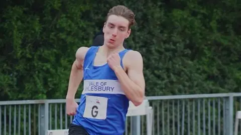 Alastair Ankers Adam Ankers wearing a blue vest and black shorts running on an athletics track