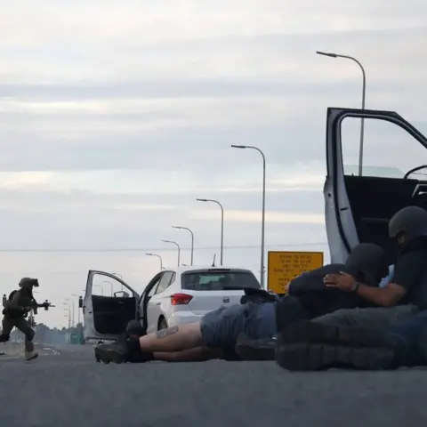 Getty Images Journalists take cover behind cars as Israeli soldiers take position during clashes with Palestinian fighters near the Gevim Kibbutz, close to the border with Gaza on 7 October, 2023