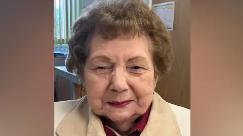 Shirley Billam smiling at the camera. She has short hair and is wearing a white jacket. 