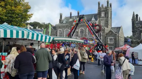 People are looking at green and white striped trade stands in front of a grand historic building.