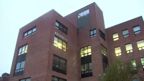 A red brick building with the windows and the words KILLYMEAL HOUSE in silver lettering on the side. 