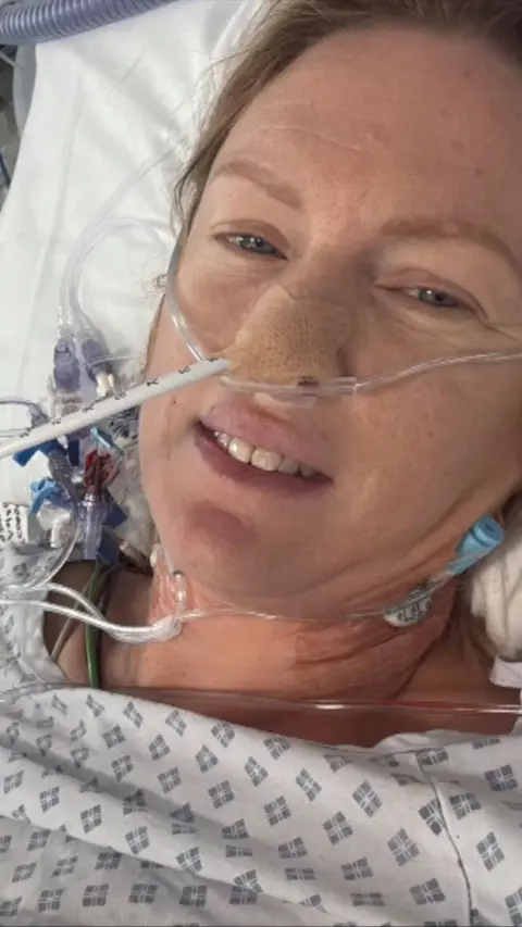 A woman in a hospital bed with breathing tubes coming out her nose.