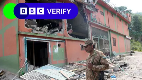 A Pakistan Army soldier stands in front of damaged Bilal Mosque after it was hit by an Indian strike in Muzaffarabad, the capital of Pakistan-administered Kashmir. He is wearing army fatigues and carrying a rifle. 