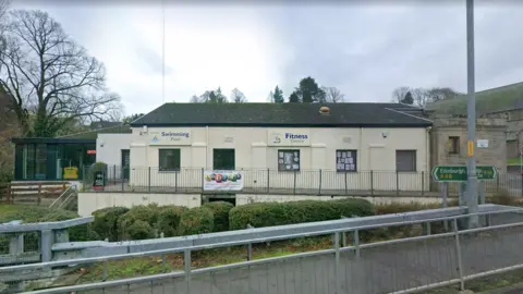 A white walled swimming pool building with signs for the swimming pool and fitness centre