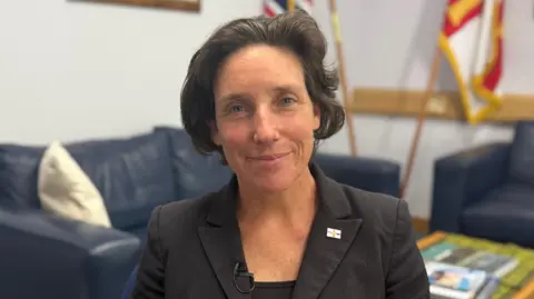 A picture of Lindsay De Sausmerez wearing a black shirt and black blazer.