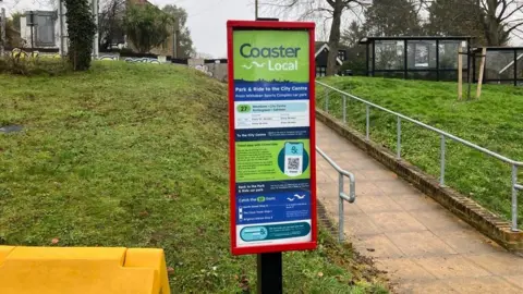 A park and ride bus board. There is green grass in the background.