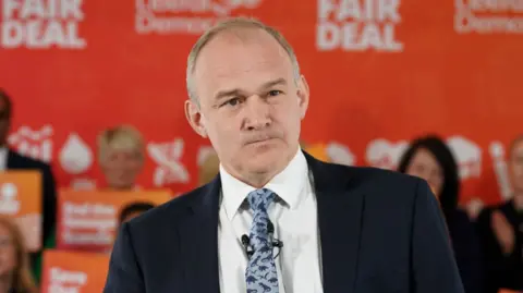 PA Media Liberal Democrat leader Sir Ed Davey speaks in front of campaigners. He wears a dark suit and a pale blue tie with silhouettes of dinosaurs.