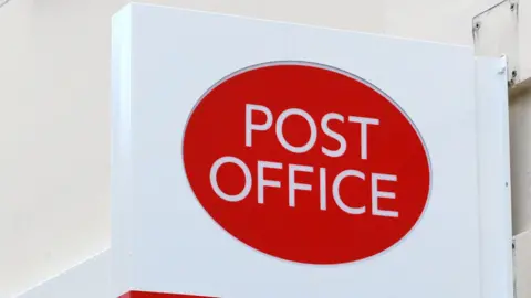 The Post Office logo, printed red and white on a sign outside.