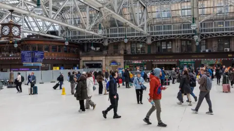PA Media the main area of Glasgow Central Station with people milling about. It has a glass roof with metal beams
