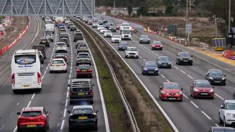 PA Media Traffic on motorway. Vehicles can be seen travelling in both directions on a three-lane road 