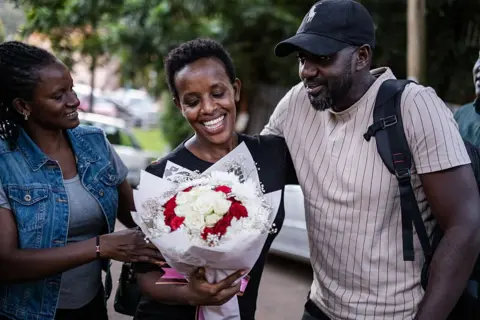 AFP / GETTY IMAGES A smiling woman is given a bouquet of flowers by people who are smiling and embracing her.