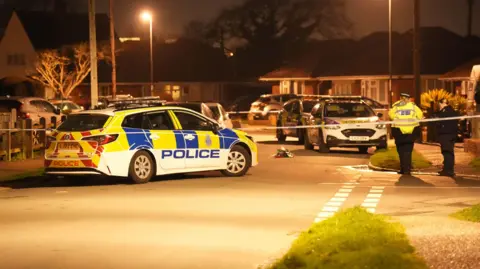Eddie Mitchell Multiple police cars are on a residential street at night. 